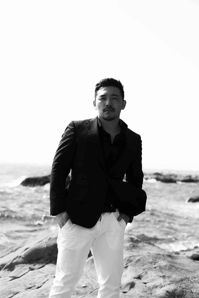 海辺の岩場に立つ、黒いジャケットに白いパンツの男性