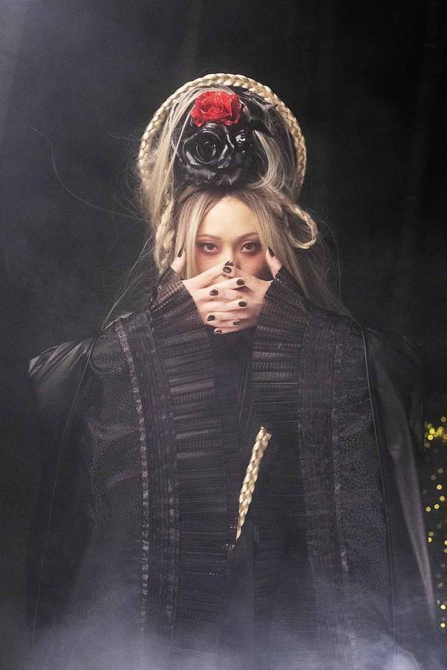 黒い衣装に薔薇の髪飾りで、口元を手で覆う女性