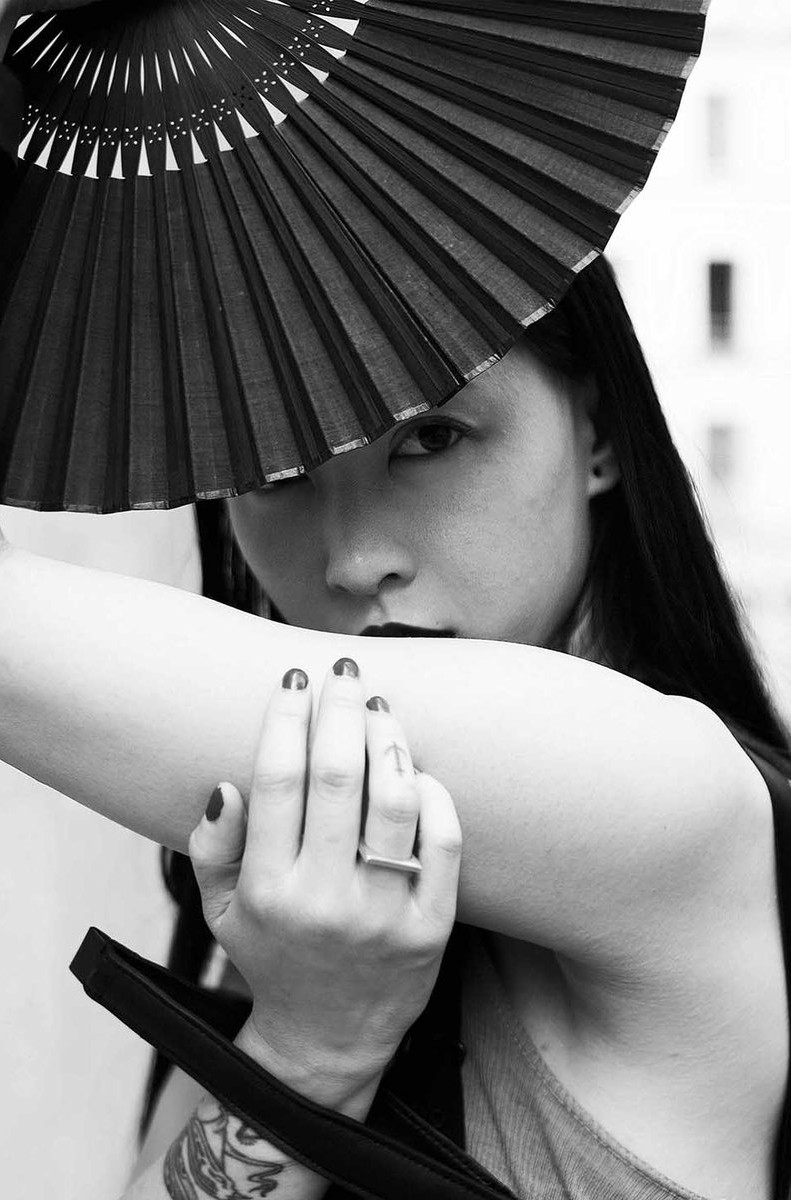 黒い扇で顔を隠す、腕に彫り物のある女性