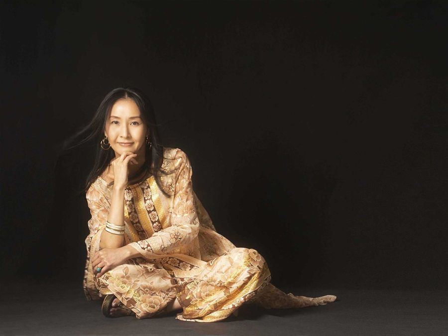 暗い背景で金の衣装をまとい座る女性
