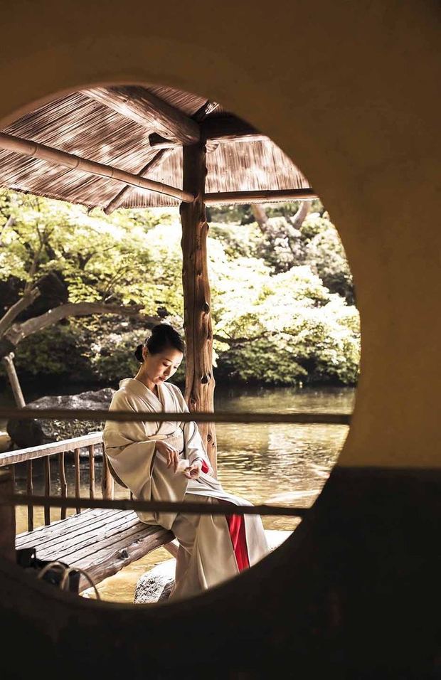 丸窓ごしに見る、水辺の東屋に座る着物の女性