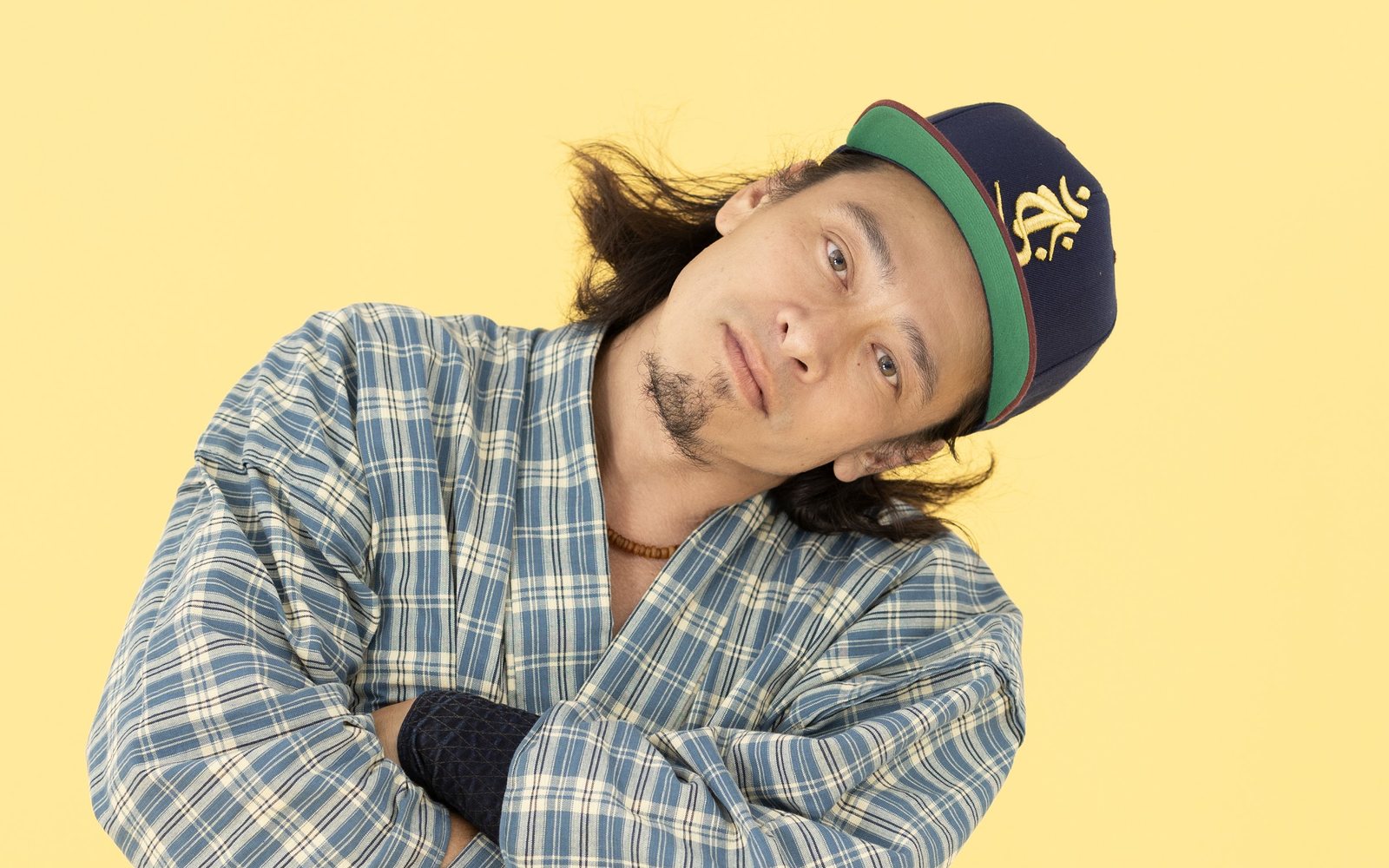 黄色い背景で、チェック柄の着物に紺のキャップを合わせた Jo Moriyama