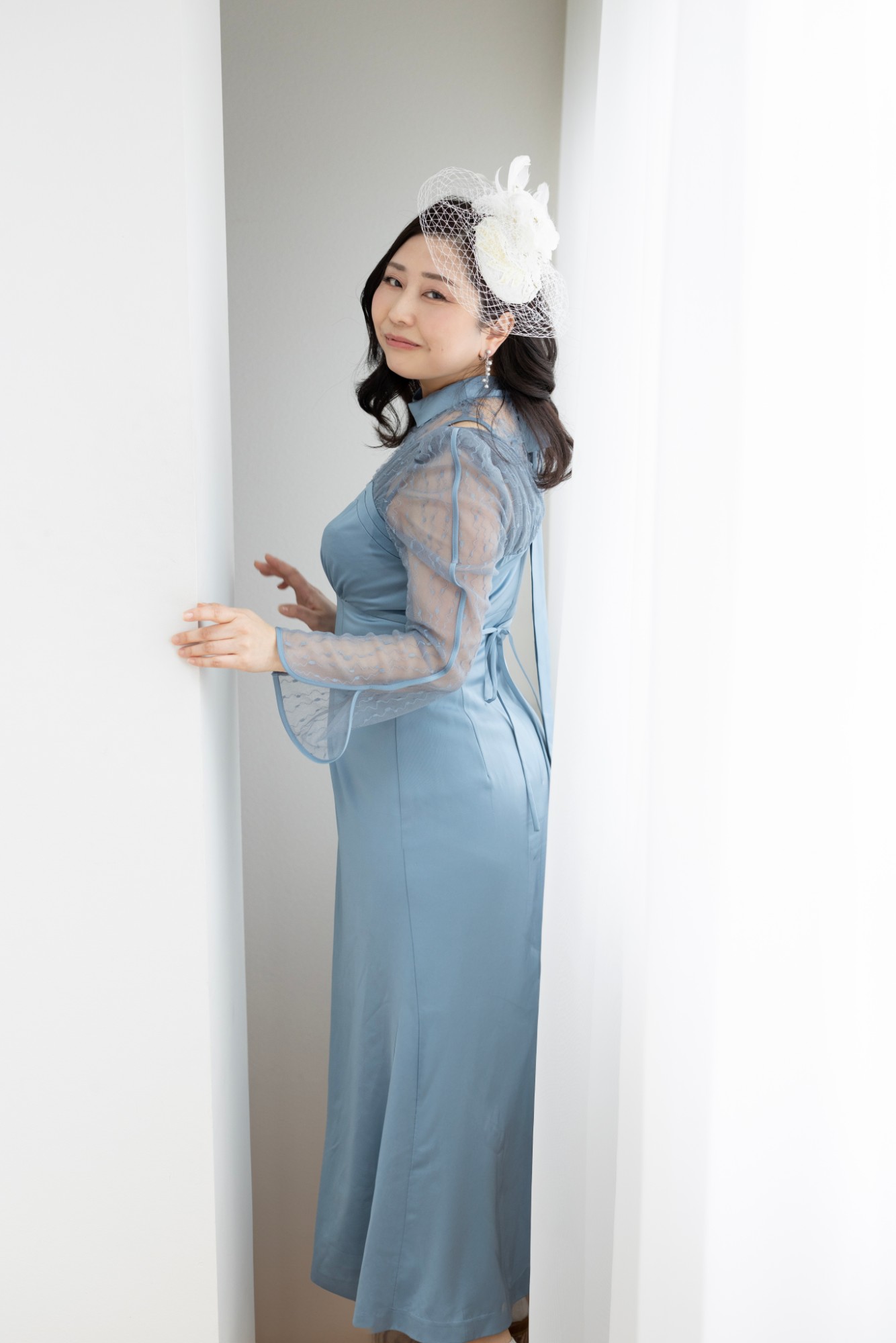 水色のドレスに白い髪飾りで、振り返ってほほえむ女性