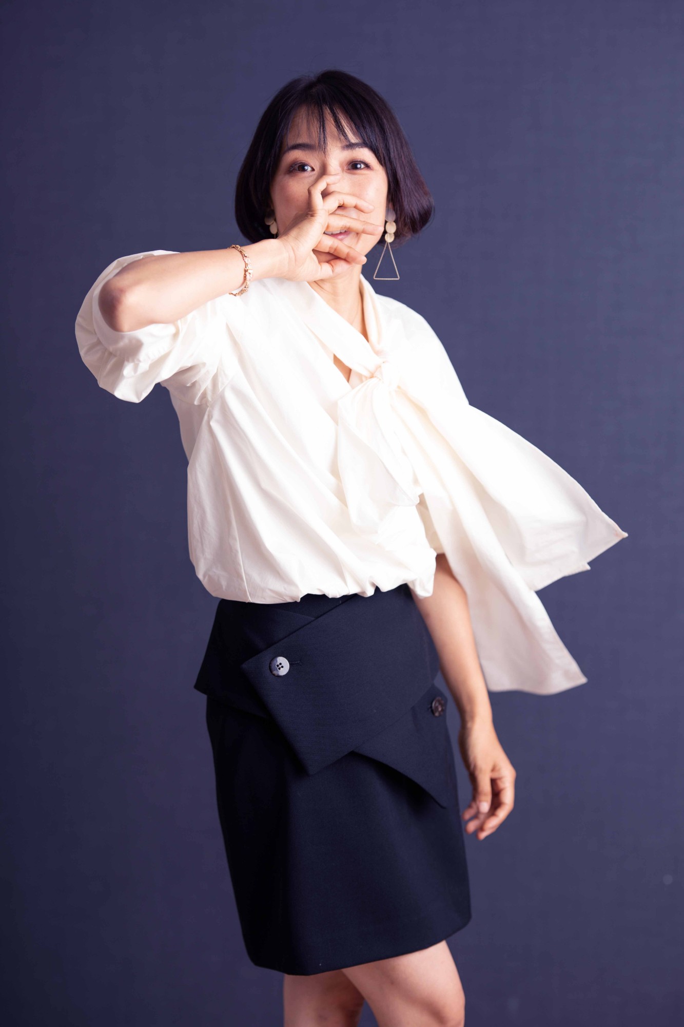 白いブラウスをなびかせ、口元に手をあてて笑う女性